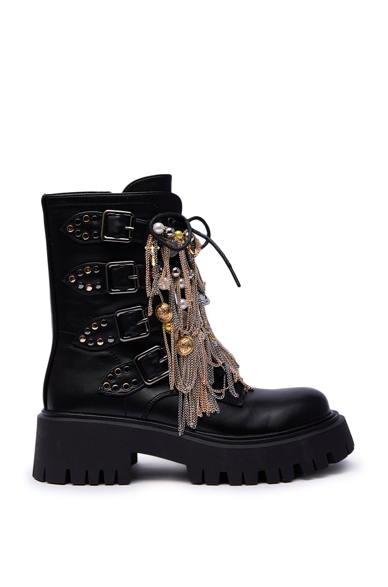 The AZALEA WANG MEGUMI BLACK METAL HARDWARE COMBAT BOOTIE features black faux leather, four side buckles, silver and gold studs, decorative chains and charms on the laces, plus a chunky heel and rugged sole for bold style.