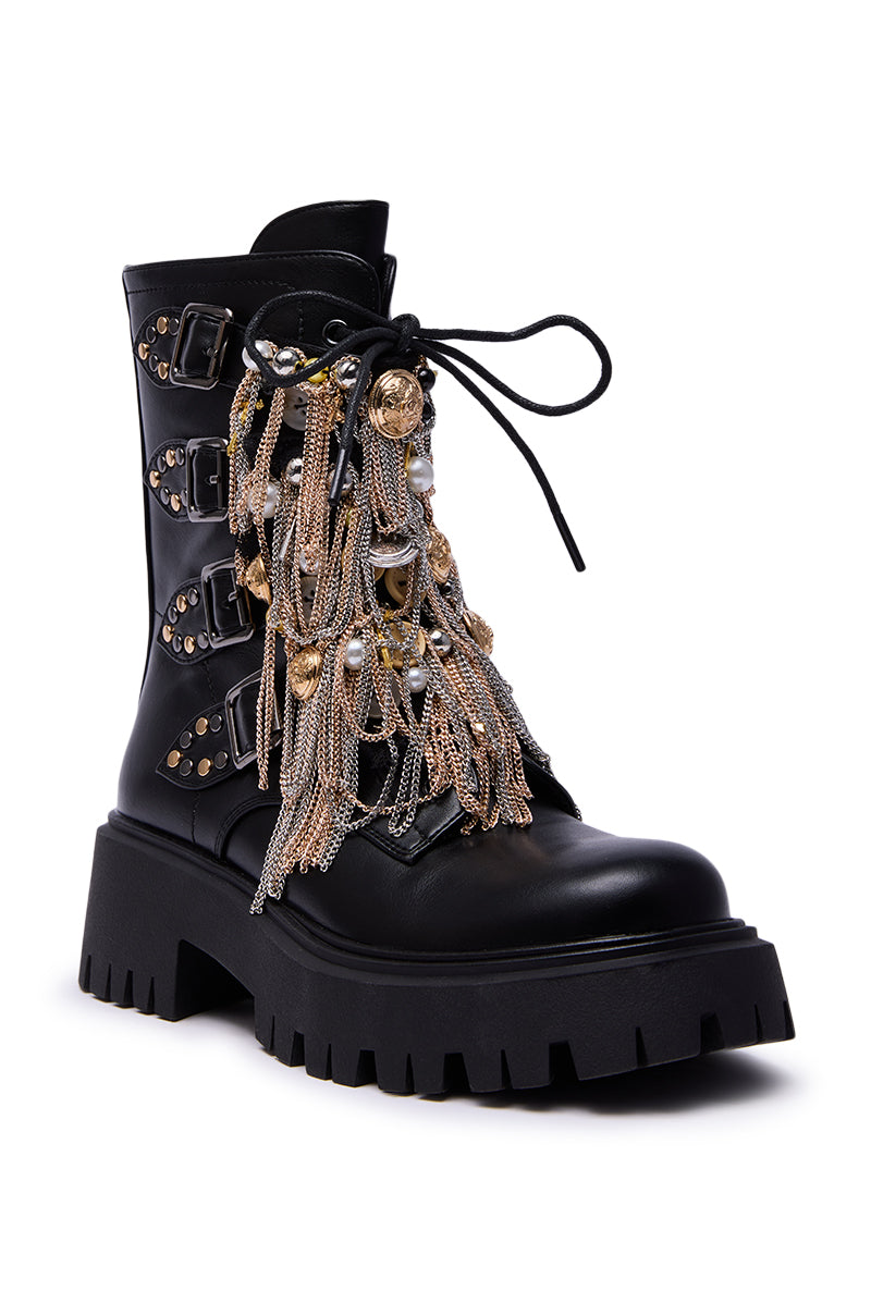 The AZALEA WANG MEGUMI BLACK METAL HARDWARE COMBAT BOOTIE features black faux leather, a chunky treaded sole, gold and silver chain fringe, metallic studs, buckles, and heart-shaped charms for an edgy look.