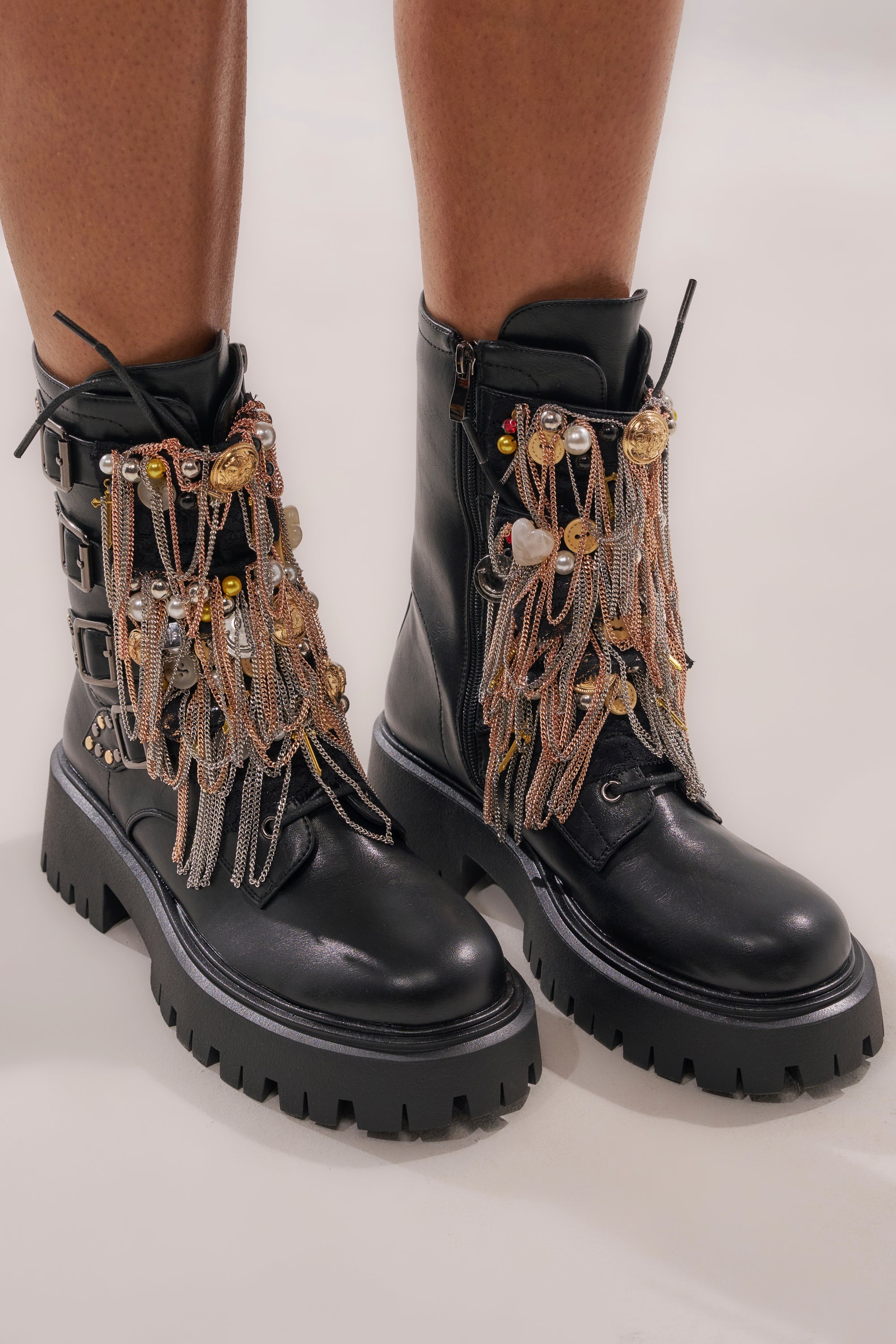 The AZALEA WANG MEGUMI BLACK METAL HARDWARE COMBAT BOOTIE is a black faux leather ankle boot with chunky soles, adorned with layered metallic chains, charms, and embellishments over the laces. 4