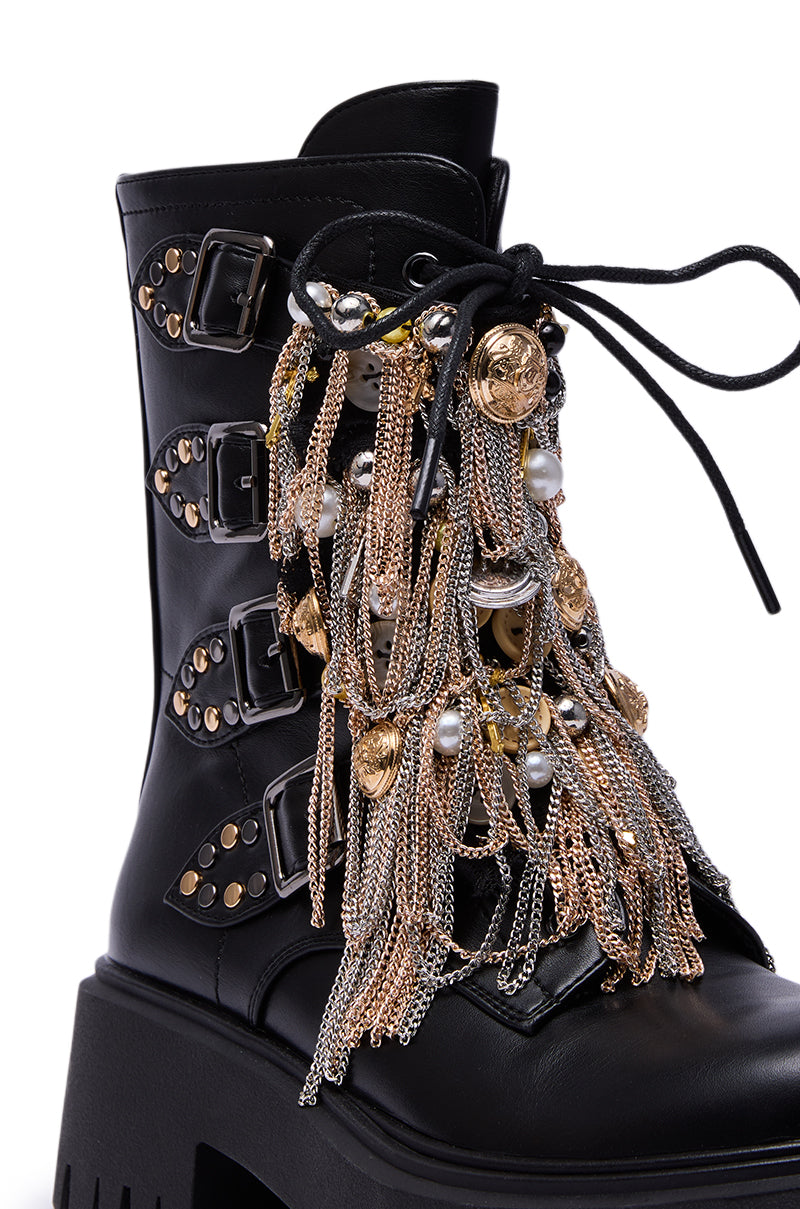 The AZALEA WANG MEGUMI BLACK METAL HARDWARE COMBAT BOOTIE features black faux leather, a platform sole, gold-tone studs, metal buckles, and draped gold and silver chains with pearls and coin charms for a bold combat-inspired look.