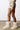 A person wearing a beige outfit features the MELANIE BEIGE FURRY BOOTIE as they stand on a polished concrete floor. The ensemble includes a cropped jacket and a mini skirt with pockets, perfectly complementing the round-toe booties against the plain white background.