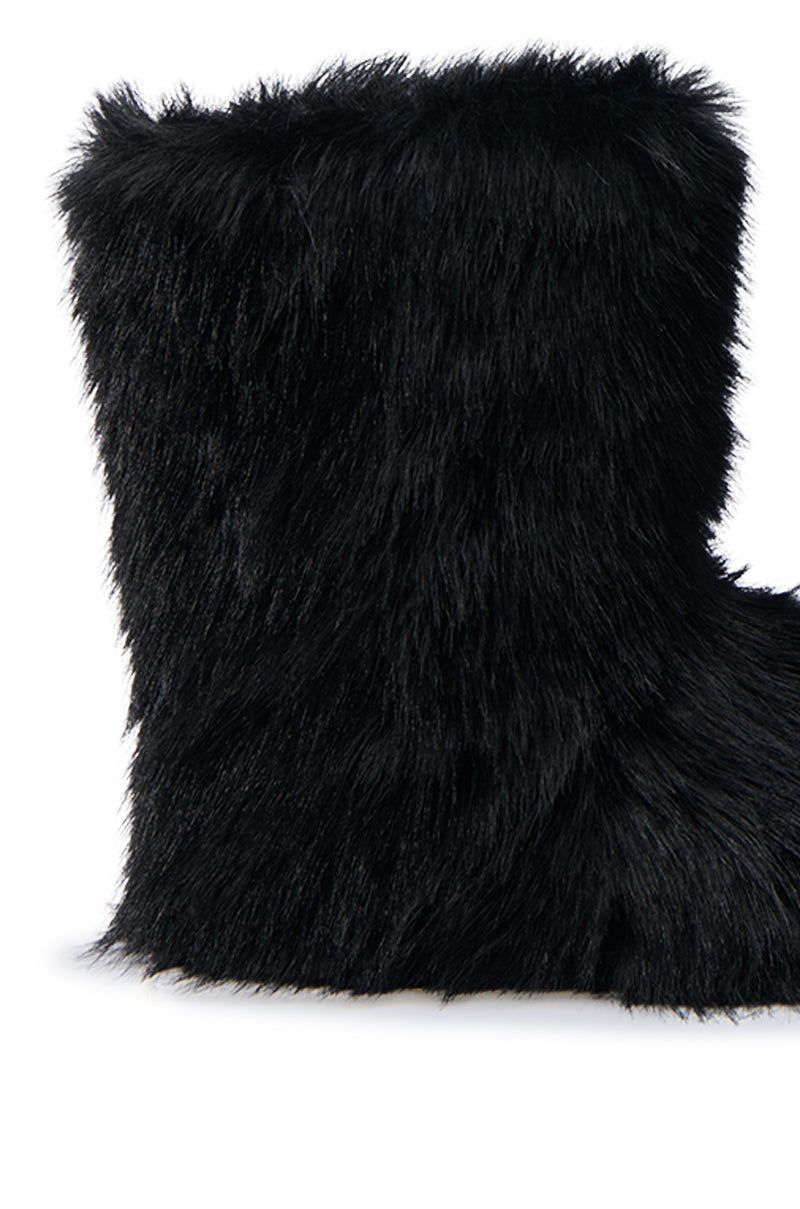 A close-up of the MELANIE BLACK FURRY BOOTIE highlights its fluffy texture. The boot extends upward, offering warmth and comfort reminiscent of a cozy ensemble. The image emphasizes the plush, faux fur appearance and meticulous design details.