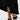 A person in a black ruffled skirt and AZALEA WANG MENES BLACK PUFF DETAIL SANDAL, featuring rectangular stiletto heels, black straps, and green bows, stands on a light-colored surface.