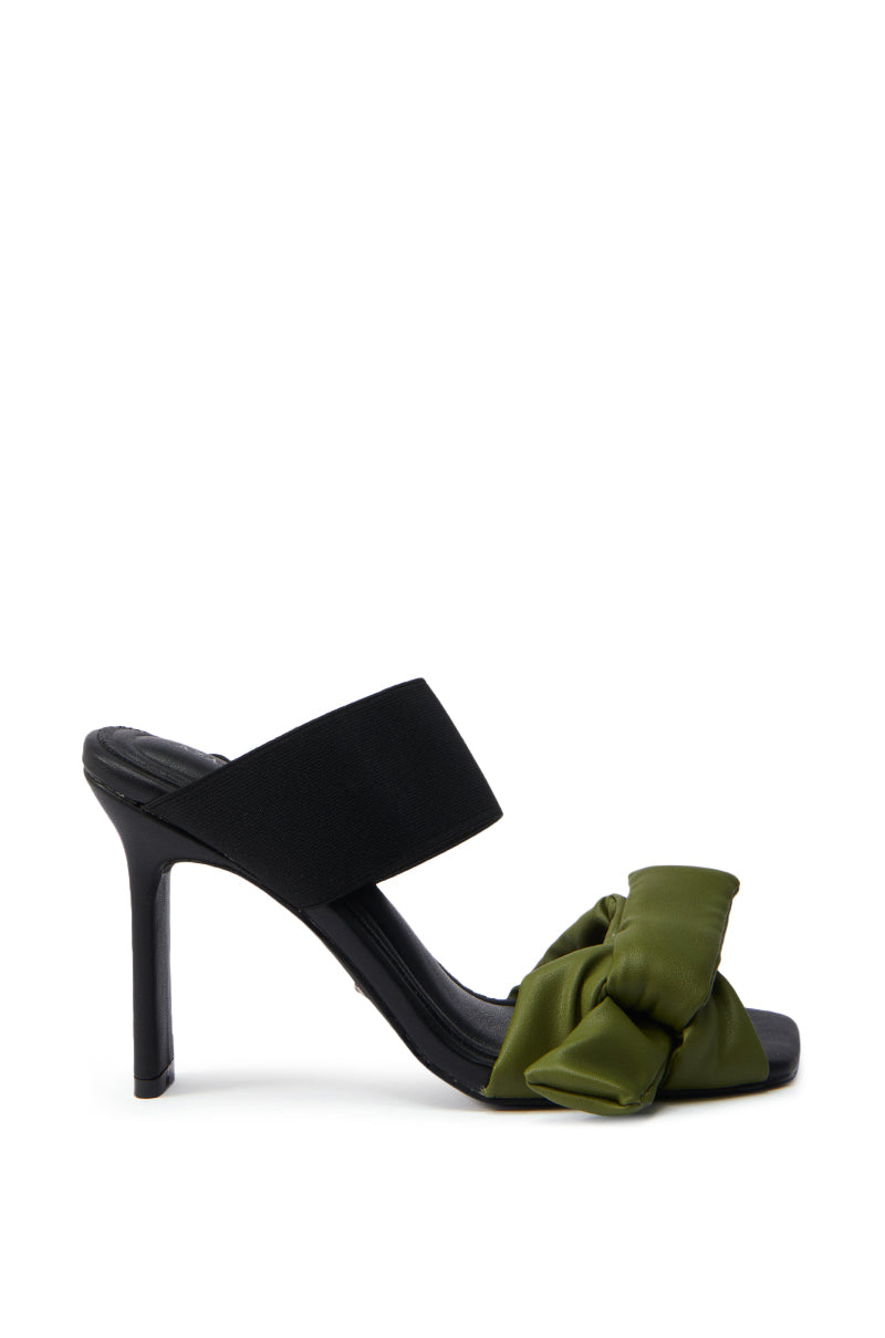 The AZALEA WANG MENES BLACK PUFF DETAIL SANDAL is a high-heeled mule with a rectangular stiletto heel, featuring two straps—one wide black and one olive green with a large fabric bow—shown on a white background.