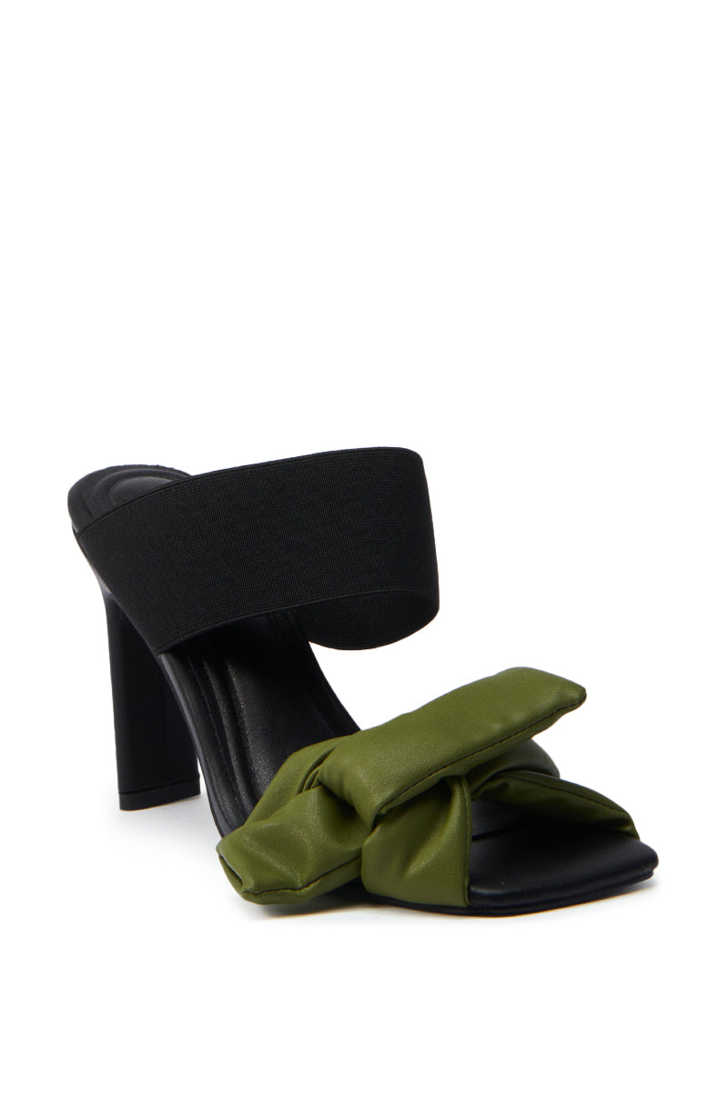 The AZALEA WANG MENES BLACK PUFF DETAIL SANDAL features a thick black stiletto heel, wide black elastic instep strap, and a green padded bow across the toe, shown on a white background.