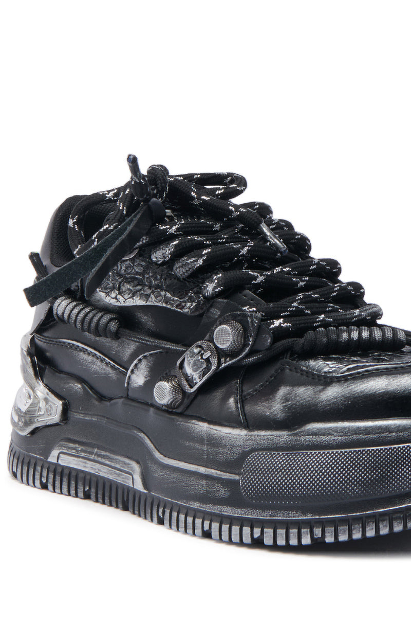 A close-up of the KOI FOOTWEAR METAMORPHOSIS BLACK FLAT DISTRESSED SNEAKER, featuring textured leather details, thick black-and-white laces, metal buckles, and a chunky sole for an industrial streetwear look with a rugged, futuristic edge. 5