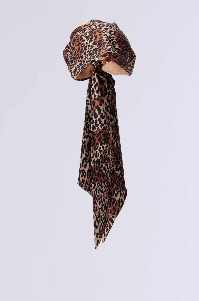 The CHEETAH ANIMAL HEAD SCARF, showcasing a leopard-print design and long, flowing tie, is elegantly displayed against a plain white background. This chic hair accessory offers versatility with its elasticized backing for a comfortable fit.