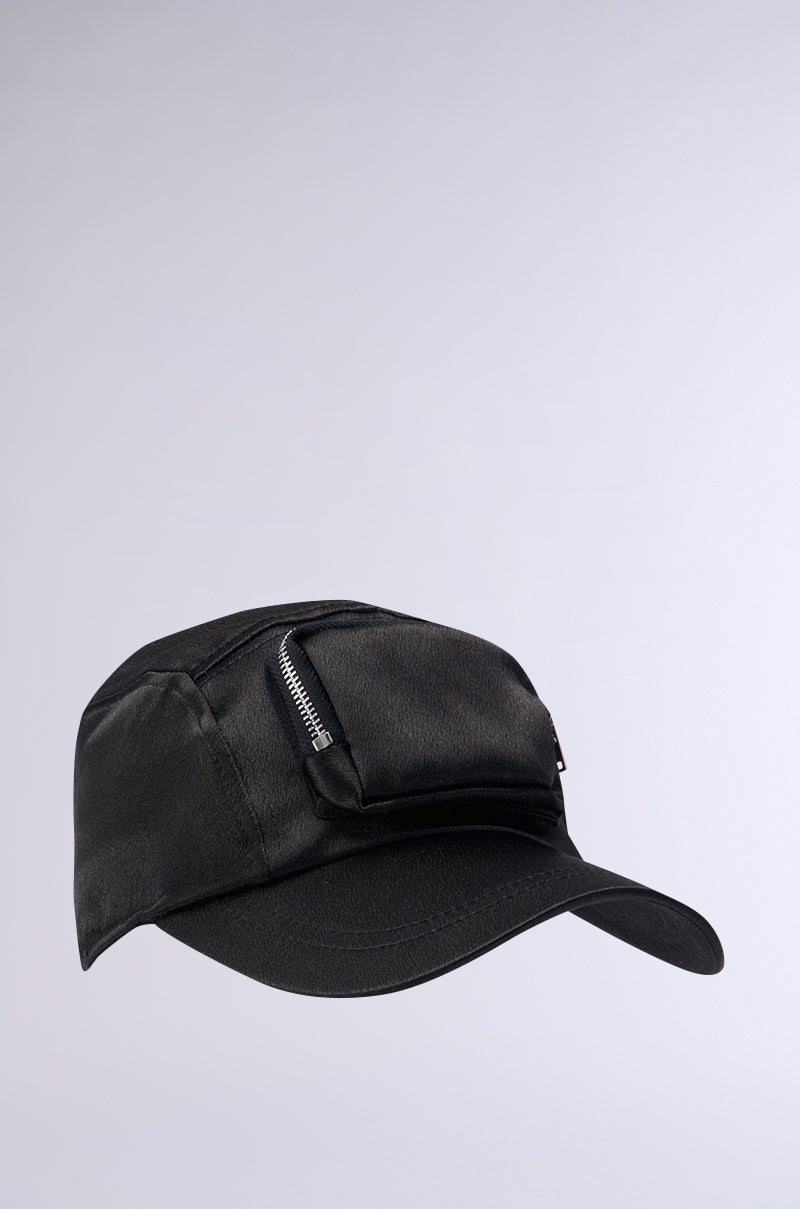 The SATIN LUXURY CARGO SNAPBACK is a black leather snapback featuring a small pocket with a silver zipper on the front left side. It has a curved brim and an adjustable velcro strap, showcasing a sleek, modern design set against a plain, light grey background. 2