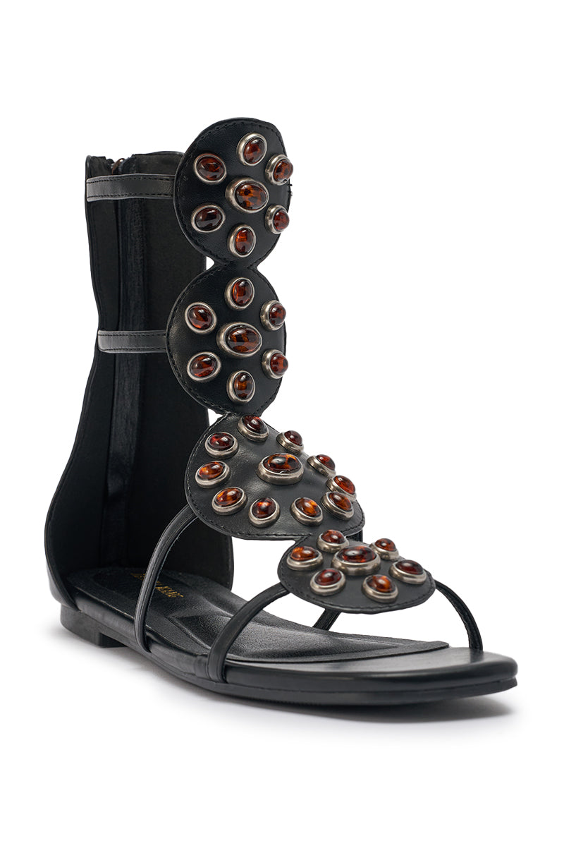 The AZALEA WANG MIKAERE sandal is a black faux leather flat with multiple upper straps, brown oval gemstone embellishments, and a back zipper closure. 5