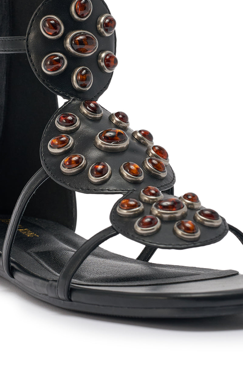Close-up of the AZALEA WANG MIKAERE BLACK BROWN STONE EMBELLISHED FLAT STRAP SANDAL, featuring circular leather panels adorned with small, amber-like stones set in metal and minimal black straps on a flat sole. 7
