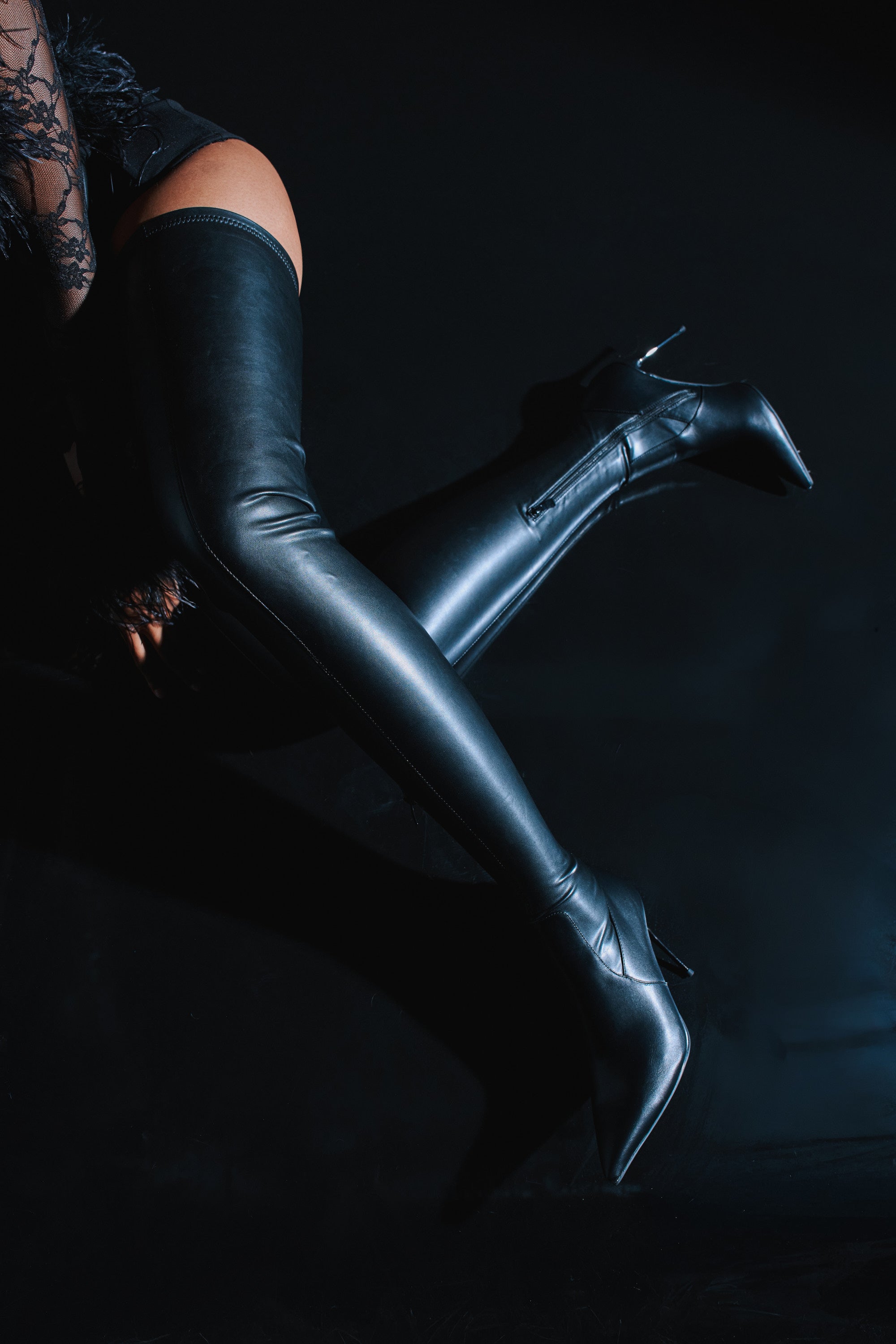 A person models the AZALEA WANG MILANDRA BLACK THIGH HIGH SEXY BOOT and lace clothing, posing against a dark background with one knee bent and the other leg extended.