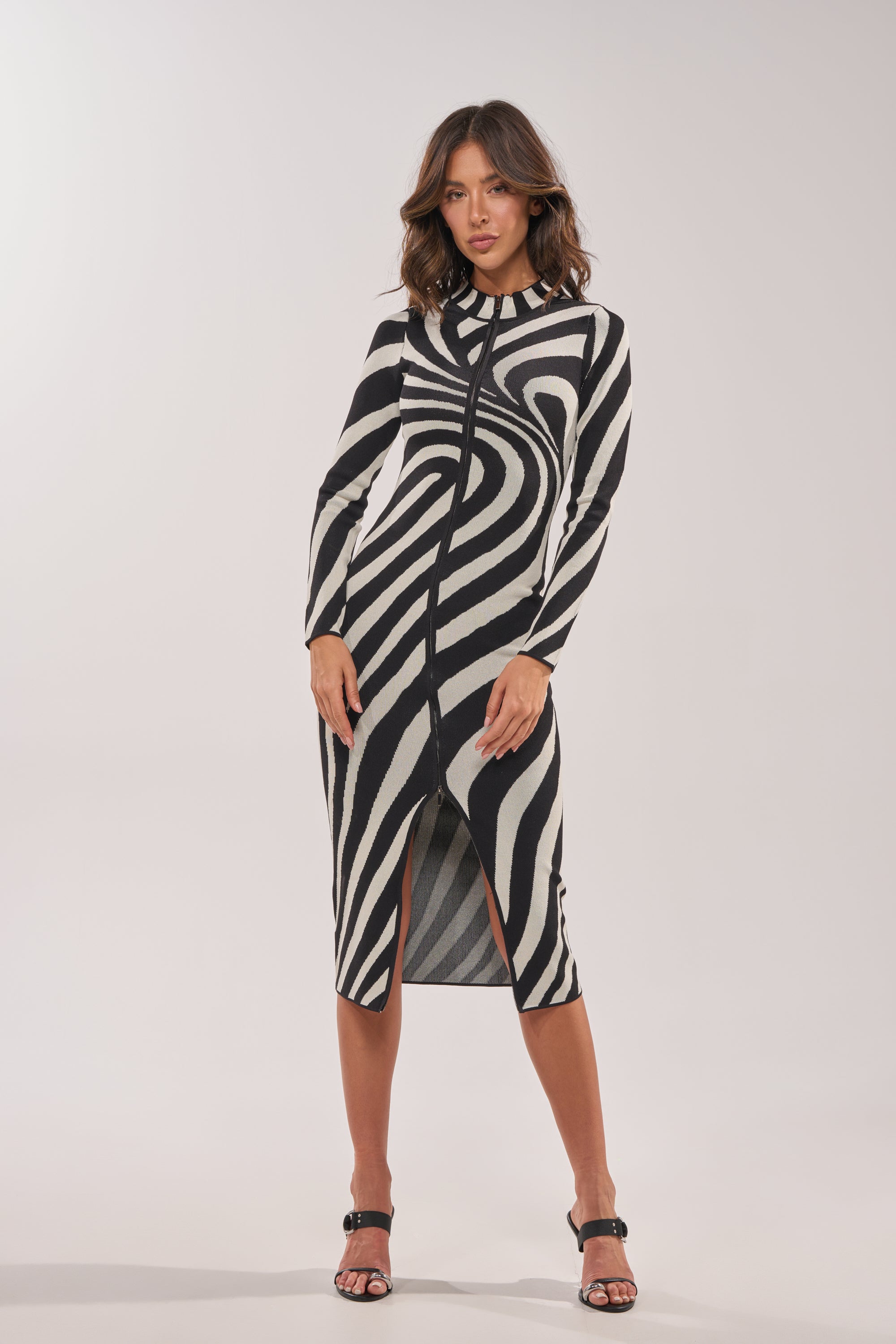 A woman models the UNDER MY SPELL MIDI DRESS—a long-sleeve, zebra-print midi dress with a front slit—paired with open-toe heels, set against a plain light background. 9
