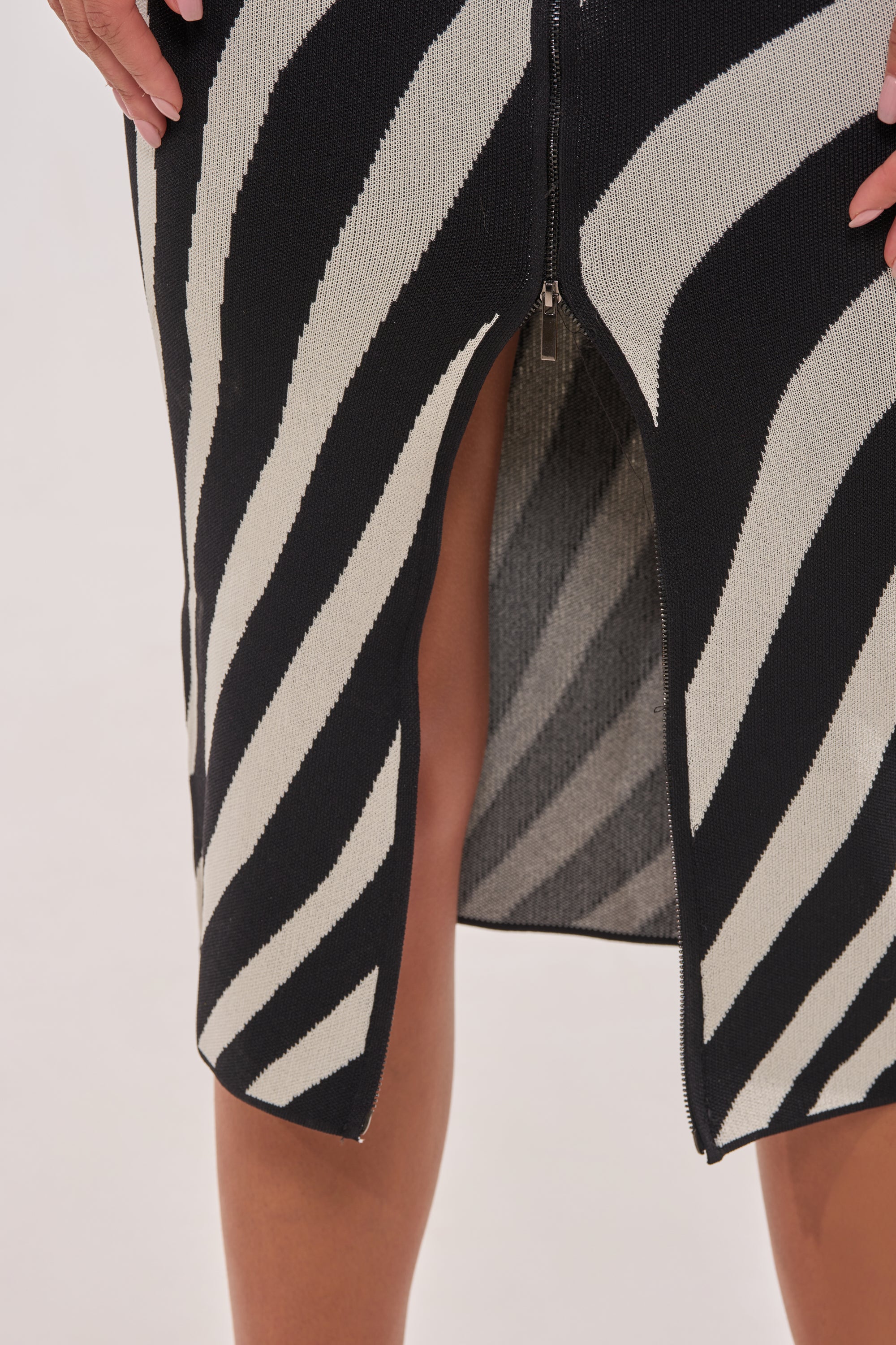 A close-up of a person wearing the UNDER MY SPELL MIDI DRESS, featuring a zebra print, front zipper, and high slit that reveals part of their legs and hands. 10