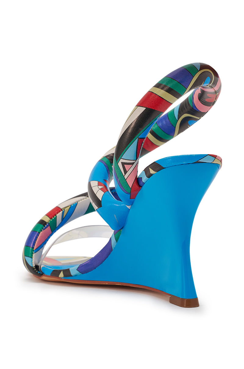 The AKIRA GOLD MINORU MULTI PRINTED WEDGE PUFF SANDAL features vibrant geometric straps, a clear side panel, and art-pop style, shown from the back angle. 6