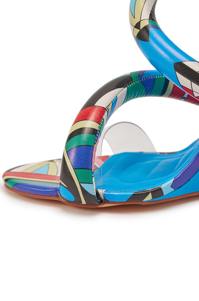 Close-up of the AKIRA GOLD MINORU MULTI PRINTED WEDGE PUFF SANDAL, featuring a colorful geometric design with blue, green, black, red, and beige accents, padded footbed, and curved straps. 7