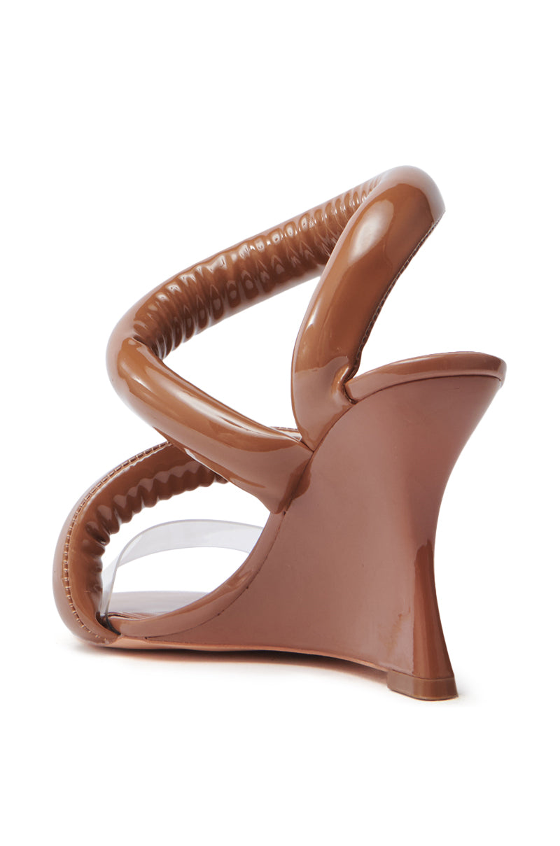 The AKIRA MINORU NUDE WEDGE SANDAL features a single brown high-heeled design in vegan patent leather, with a unique twisted strap, transparent front strap, curved heel, glossy finish, and comfort cushion insole for lasting wearability.
