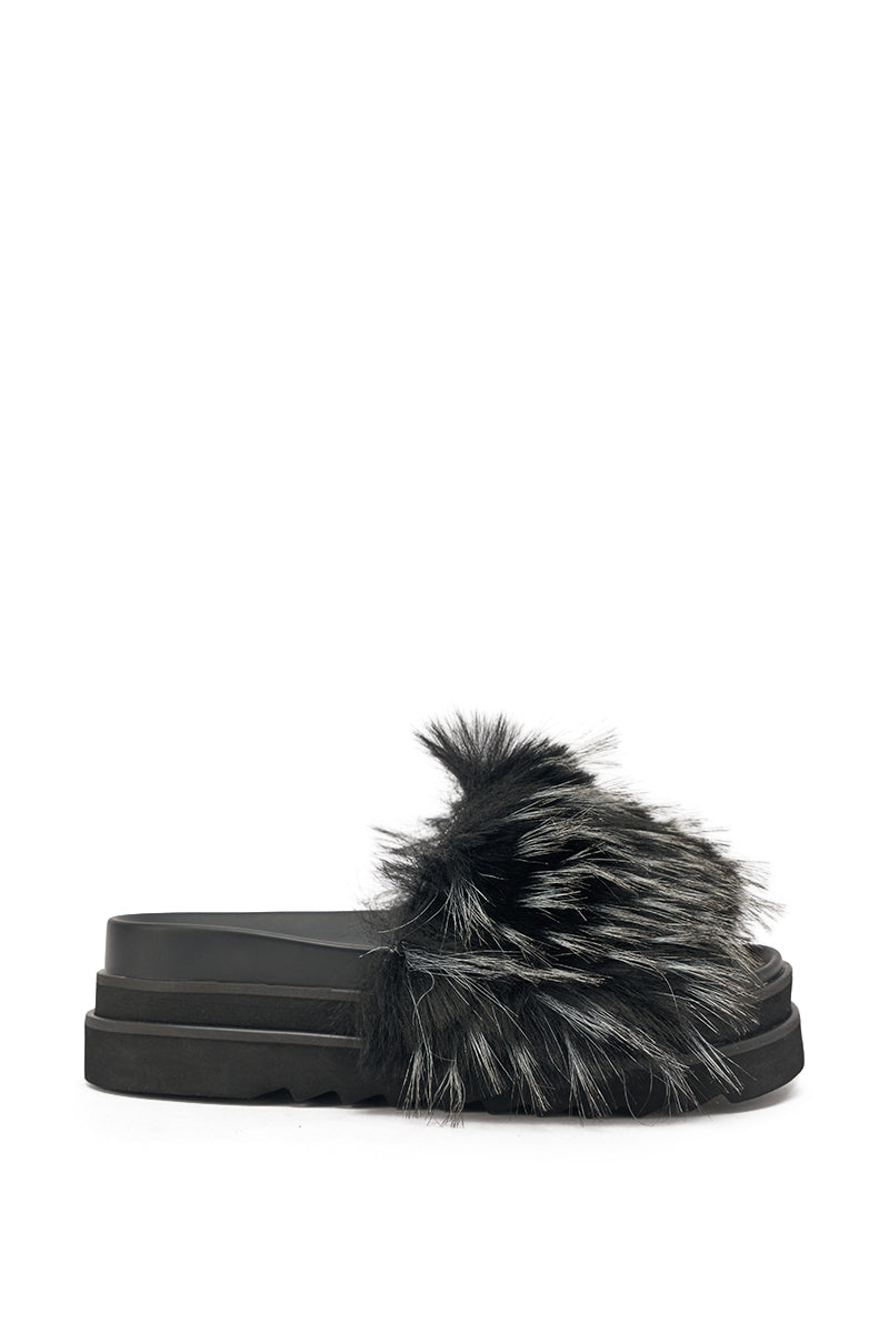 The AKIRA MIRAY BLACK MULTI BLACK FUR SLIDE is a faux leather platform sandal with a thick, chunky sole and a large black-and-white streaked faux fur strap. The slide is displayed side-on against a plain white background. 3