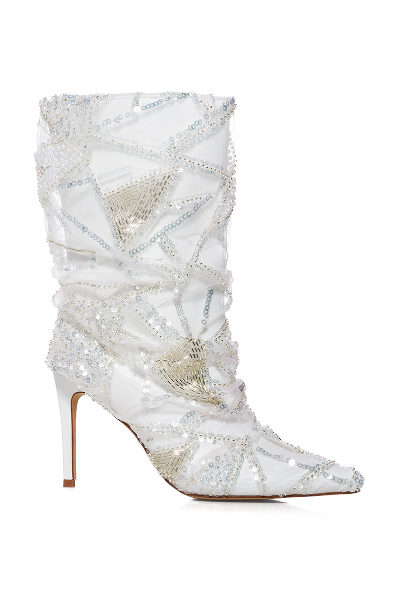 The AZALEA MITSKI WHITE SEQUIN OVERLAY BOOTIE features a faux leather upper with intricate beadwork and sequins, forming a shimmering design. It's a white high-heeled bootie with a pointed toe and mid-calf height complemented by a slim heel.
