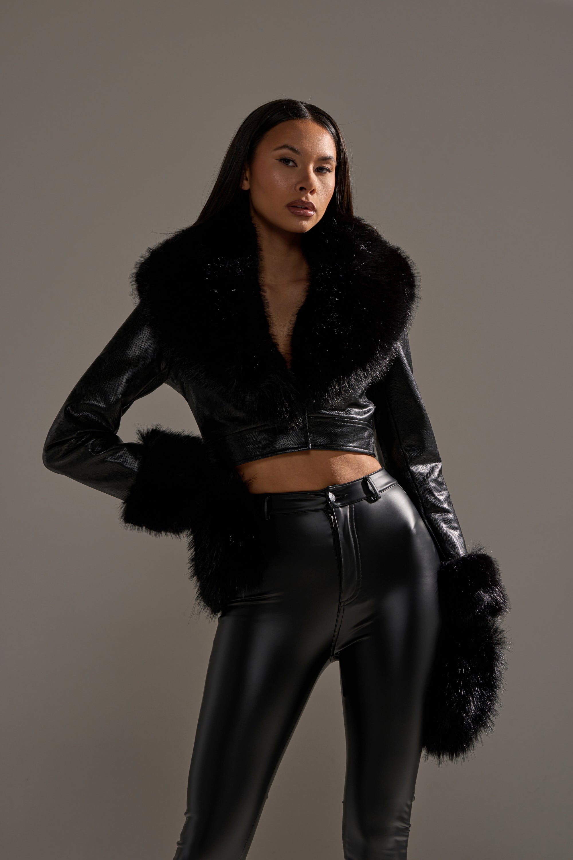 A woman poses confidently in chic black leather attire, completing her winter look with cozy IN THE NIGHT FAUX FUR MITTENS, set against a neutral background. 2