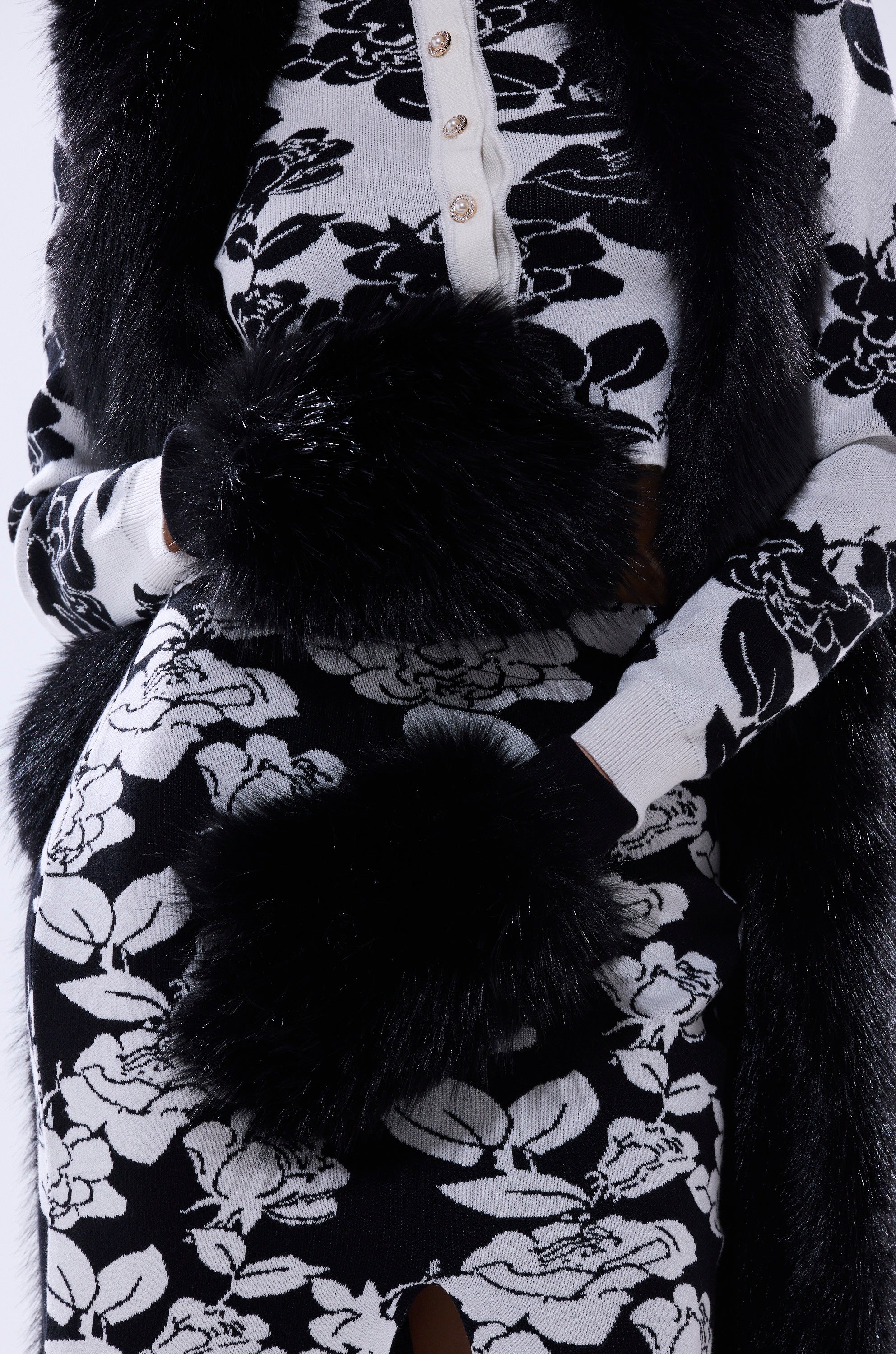 A person wears black-and-white floral attire accented with shiny faux fur cuffs, featuring the IN THE NIGHT FAUX FUR MITTENS—a standout winter accessory pairing large flower prints with cozy texture. 4