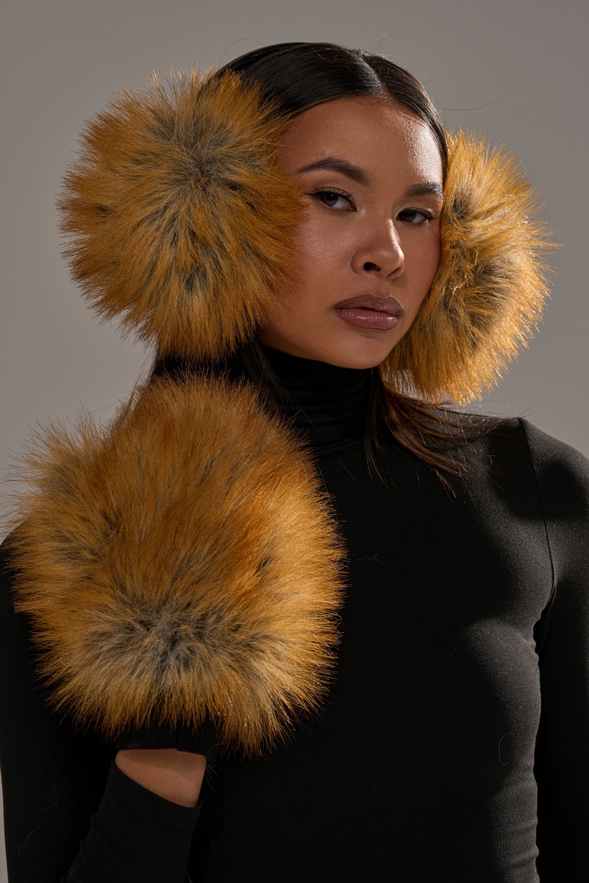 A woman in a black turtleneck poses against a neutral background, wearing REALLY LIKE THAT FAUX FUR MITTENS—large, plush orange-and-black faux fur accessories on her wrists and matching earmuffs. 0