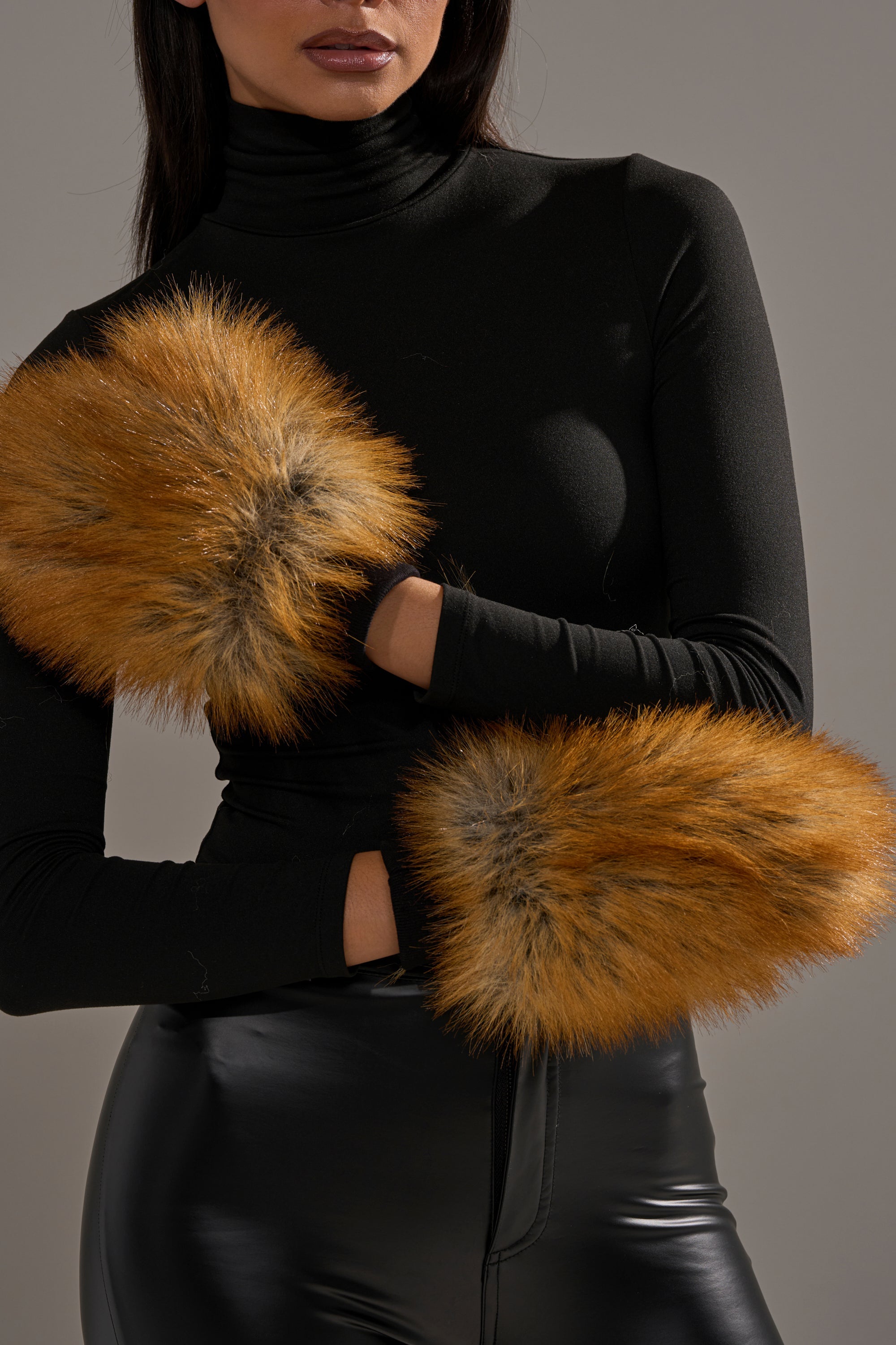 A woman in a black turtleneck and leather pants models REALLY LIKE THAT FAUX FUR MITTENS on her wrists, arms crossed against a plain background—a chic touch for any winter wardrobe. 1