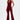 A woman wears the LIKE MAGIC JUMPSUIT IN BURGUNDY, featuring a draped neckline and flared legs, styled with gold platform heels against a plain white background.