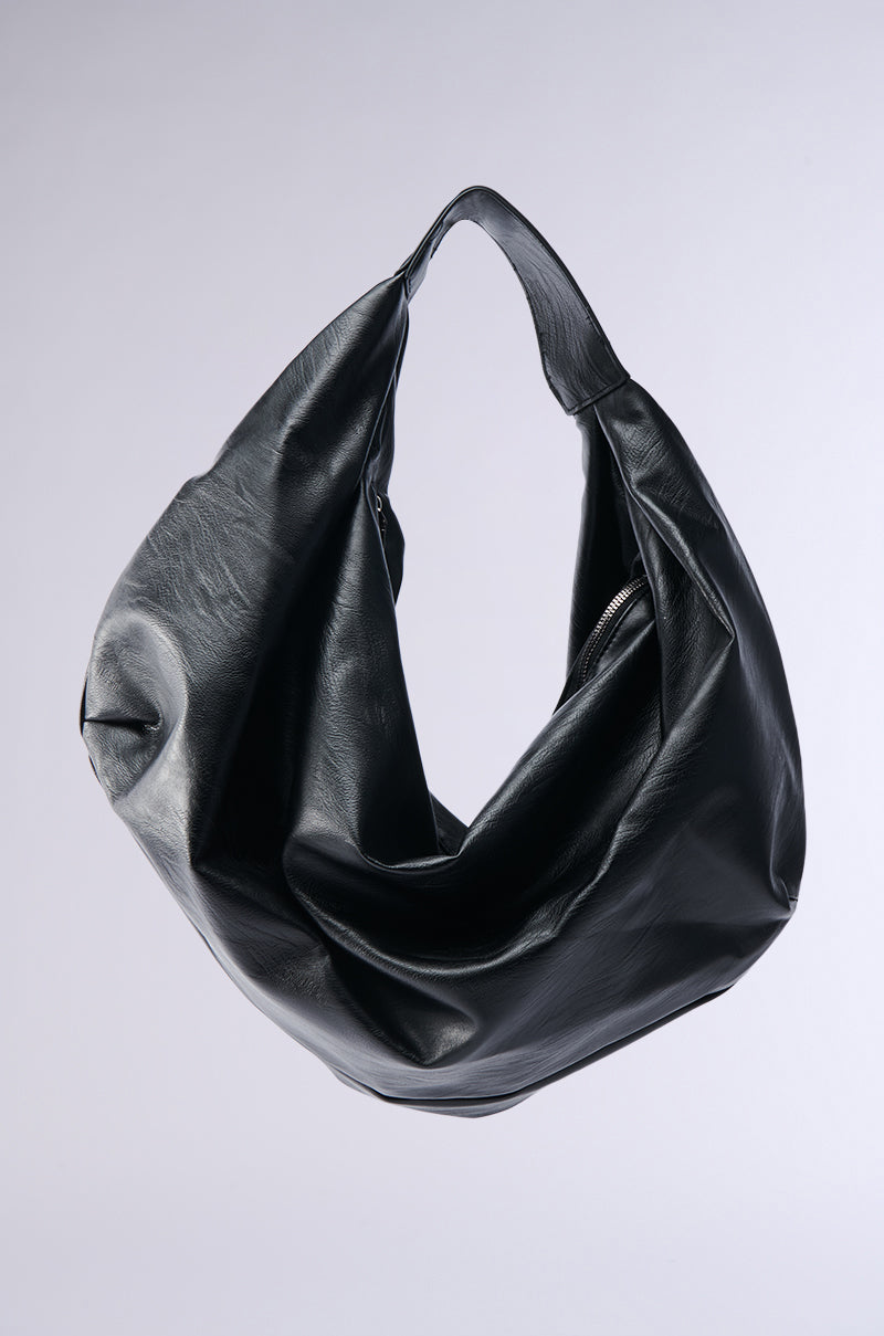 The EDITORIAL ONLY TOTE is a large, slouchy black leather hobo-style bag with a wide strap, shown against a light gray background—ideal for minimalist looks.