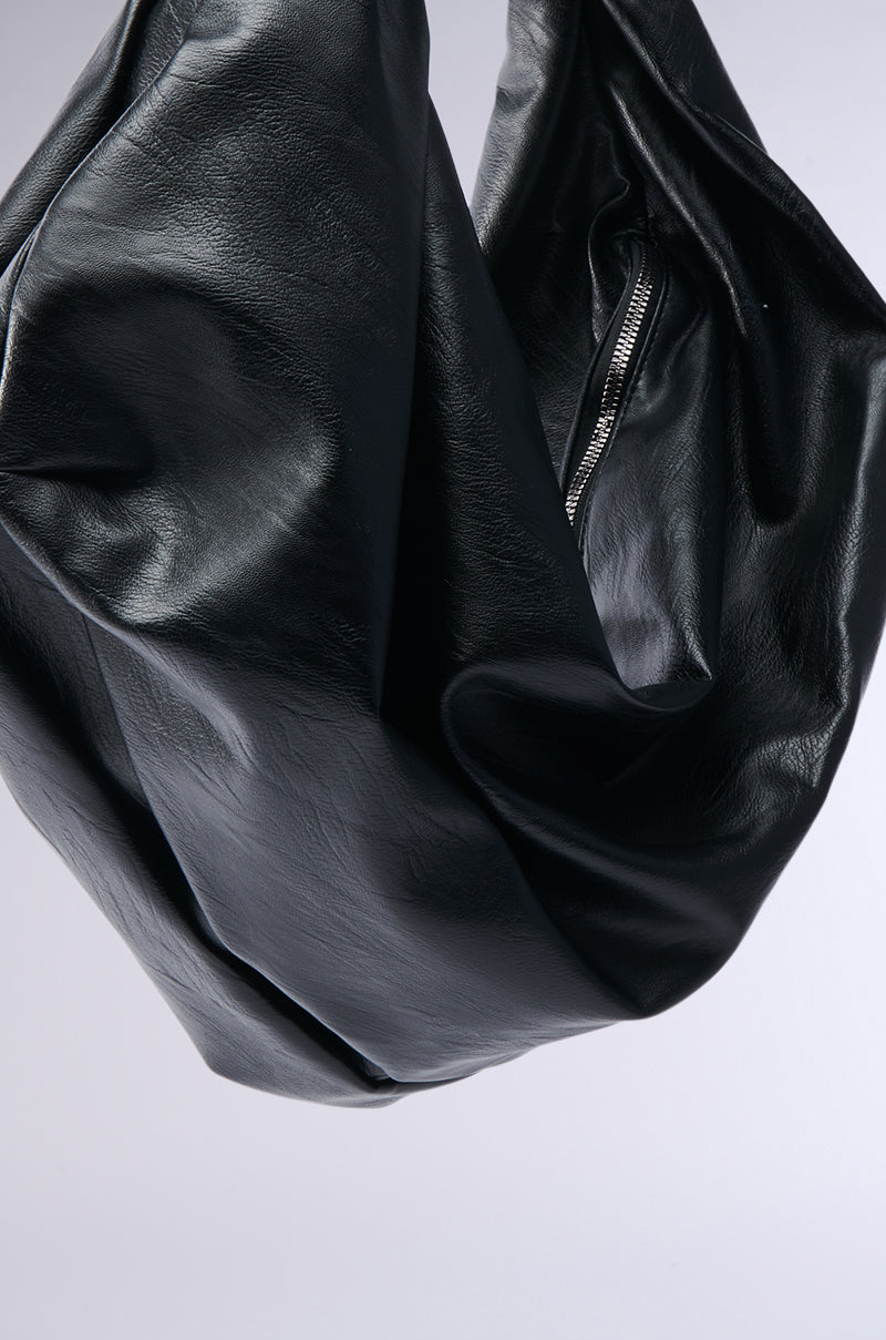 A close-up of the EDITORIAL ONLY TOTE, a black faux leather handbag with a visible zipper, photographed on a plain light gray background—ideal for minimalist styles.