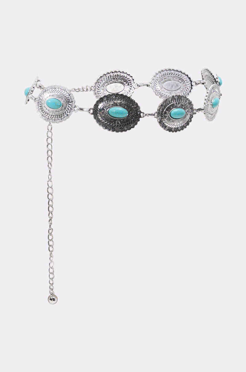 The LETS ROCK CHAIN BELT is a silver Western accessory featuring ornate oval conchos with engraved details and turquoise stones, linked in a row and finished with an adjustable dangling chain.