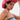 A person with short dark hair sports the ROSES ARE RED COWBOY HAT with white floral designs, a nose ring, and a strapless denim top. A bold maroon stripe tattoo accents their shoulder as they look confidently at the camera.