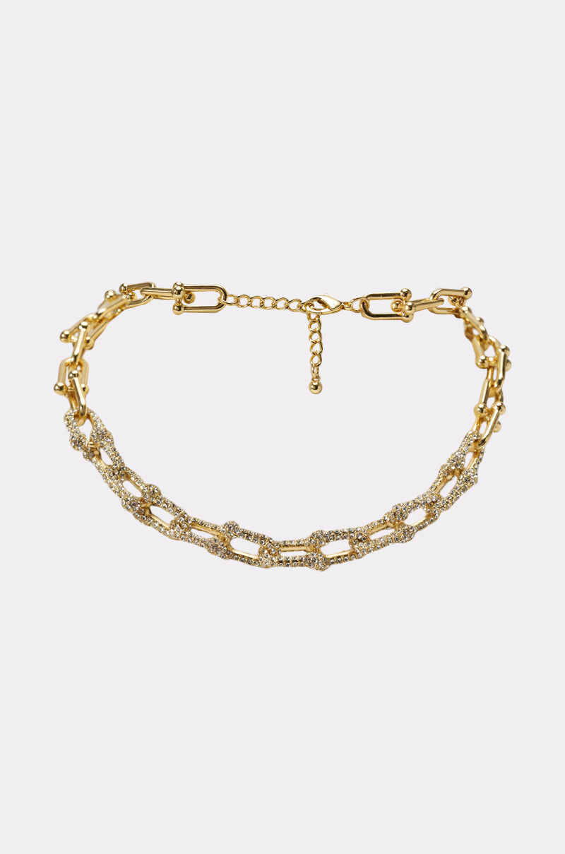 The LUXE LIVING GOLD NECKLACE is a statement piece with two layered chains—one with plain links and the other adorned with sparkling rhinestones—set against a simple white background. 1
