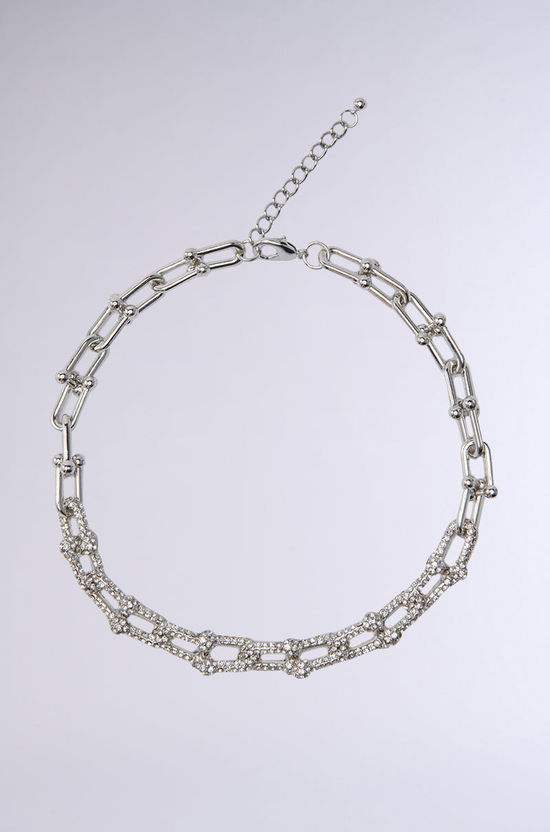 The TIFF NECKLACE is a silver chain-link statement piece with rectangular links, a rhinestone-embellished section, and an adjustable extender clasp, displayed on a light gray background. 0
