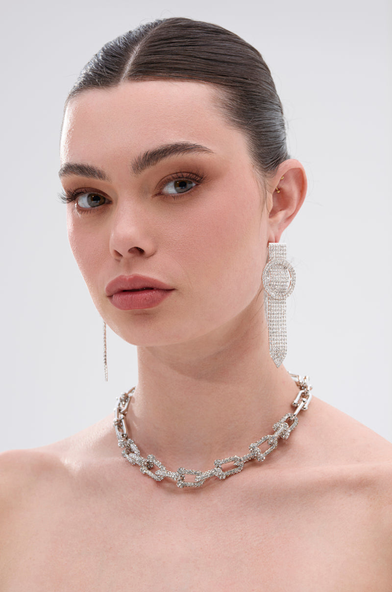 A woman with fair skin and dark hair pulled back models the TIFF NECKLACE and diamond earrings. Wearing natural makeup, she gazes just past the camera against a plain, light background. 2