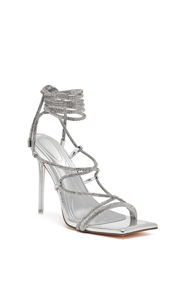 The AZALEA WANG MOEY SILVER STILETTO SANDAL features a square toe, thin rhinestone straps, a wraparound ankle tie, and a sleek metallic heel, stylishly displayed against a white background.