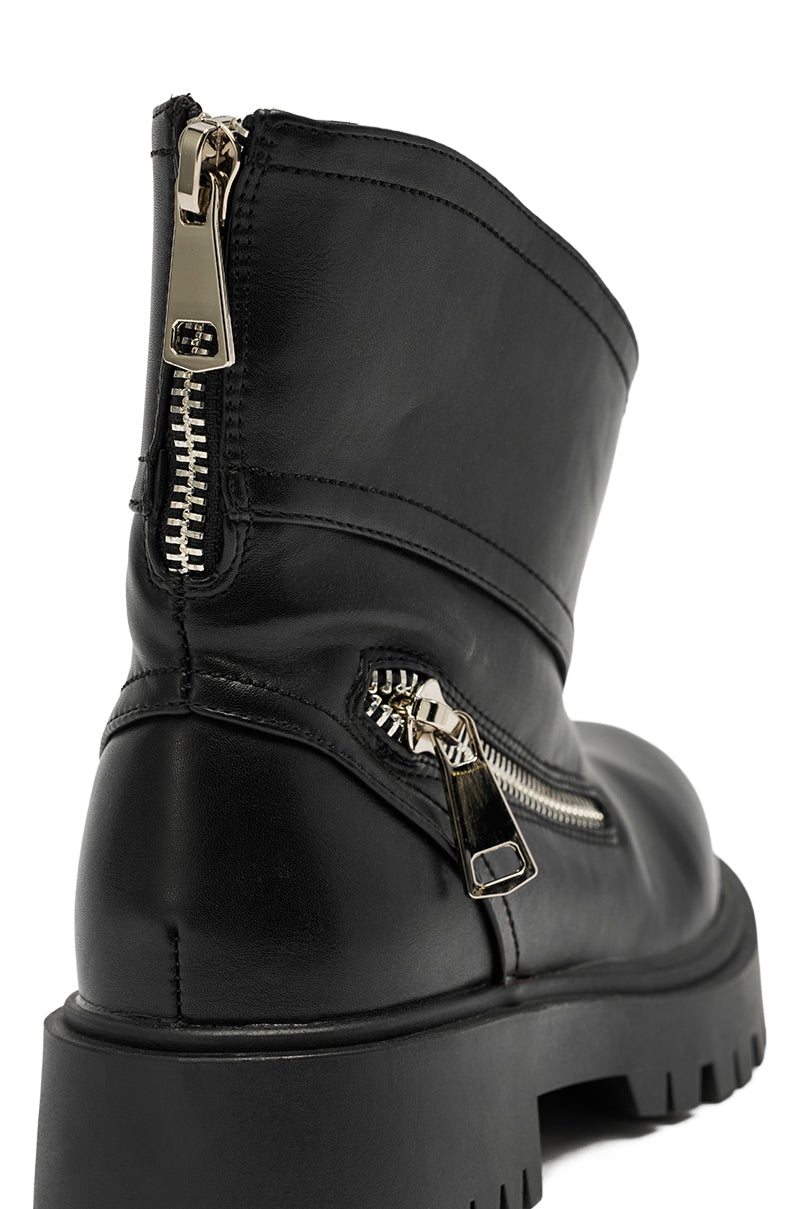 Close-up of the AZALEA WANG MOHSEN BLACK COMBAT BOOTIE in faux black leather, featuring a chunky sole and two metallic zippers—one on the side and one at the heel—with gold-tone zipper pulls.