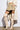 A person is wearing a cream trench coat over a cropped white top and beige pleated mini skirt, completed with MONTAGE BEIGE STILETTO BOOTS featuring thigh-high design and sculpted stiletto heels, creating a modern ensemble against a plain background.