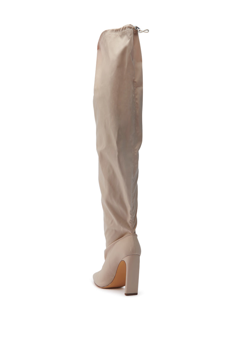 The MONTAGE BEIGE STILETTO BOOT, a knee-high masterpiece with a smooth texture and drawstring top closure, stands elegantly against a white background. Its sleek design and sculpted stiletto heel enhance its sophisticated charm.