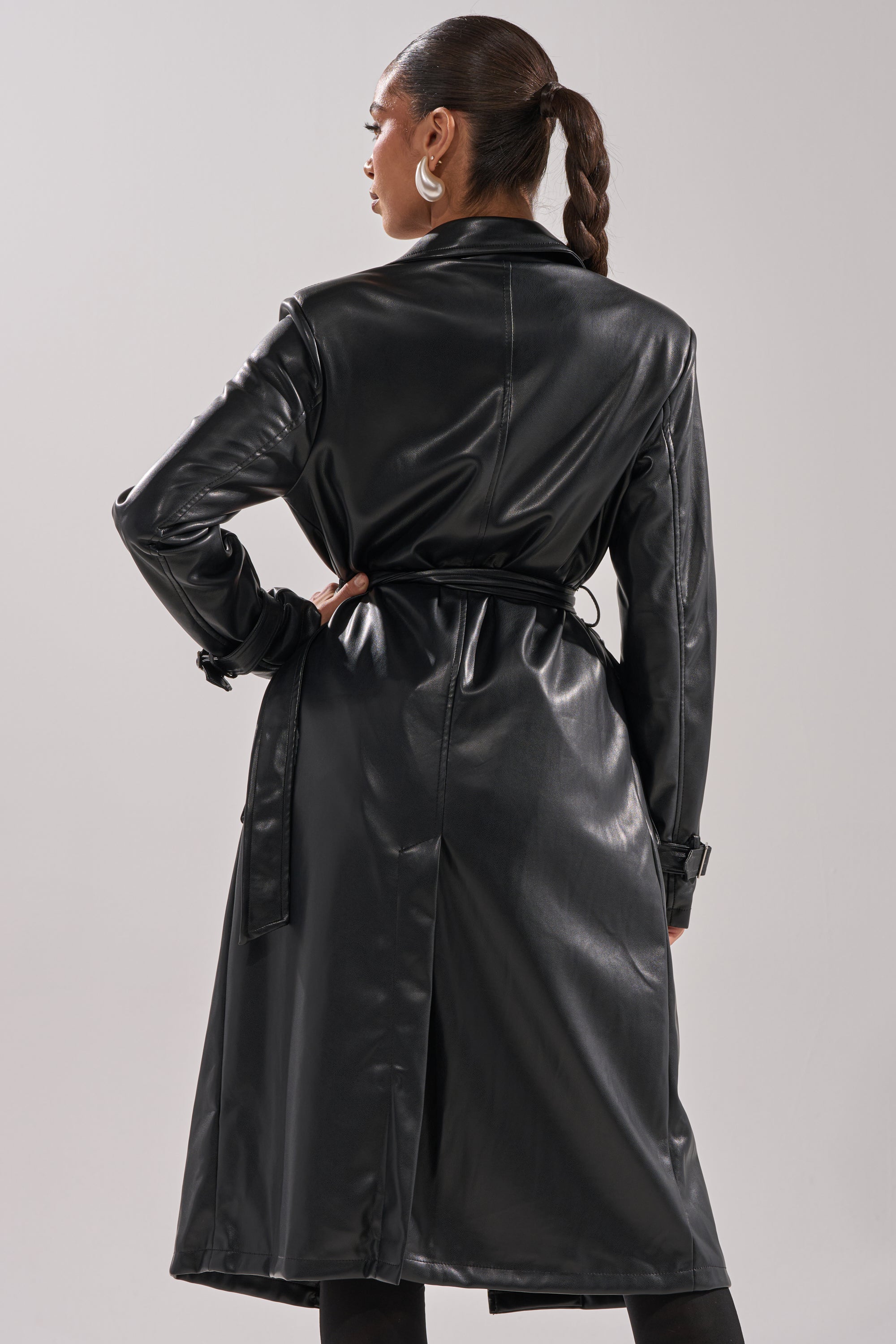 A person with a braided ponytail, seen from the back, wears the MONTANNA BUTTER LUXE EVERYDAY TRENCH tied at the waist with large hoop earrings—a true minimalist statement coat. 4