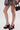 A person in a leopard print skirt, AZALEA WANG MORITZ BLACK SPIKEY WEDGE SANDALS with platform soles, and a small black handbag stands against a plain white background for a bold punk-glam look.