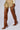 A person wearing a beige mini skirt and the AZALEA WANG MOSSY TAN BOOT, a pair of high-heeled, thigh-high brown leather boots with a side zipper. The background is plain and light-colored. The outfit emphasizes the boots and skirt, showcasing a stylish and bold fashion choice.