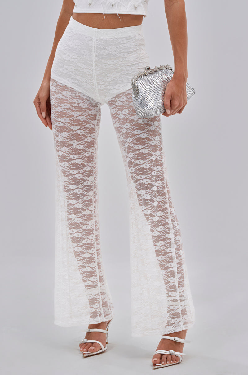 Wearing the HOT STUFF LACE FLARE LEGGING as festival bottoms with a cropped white top, white heeled sandals, and a sparkly silver clutch purse against a plain background. 1