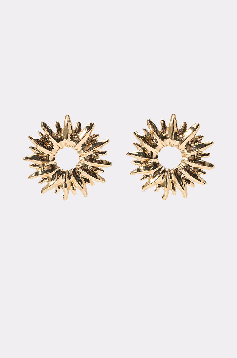The SUNBURST EARRING features metallic gold, textured radiating spikes and a circular open center—ideal wedding guest accessories—shown against a plain light background. 0