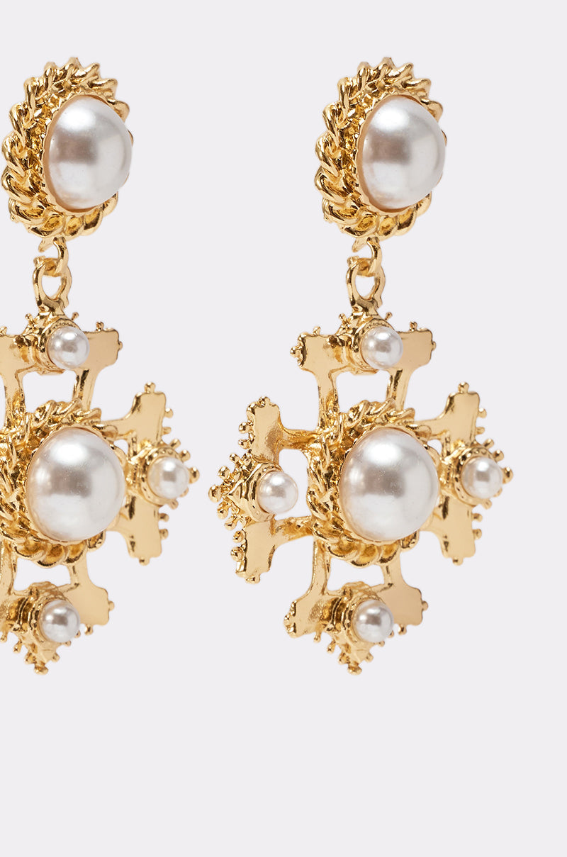 Close-up of CROSS MY HEART EARRING, ornate gold dangle earrings with large and small round white pearls, intricate gold detailing, and textured edges on a light background. 4