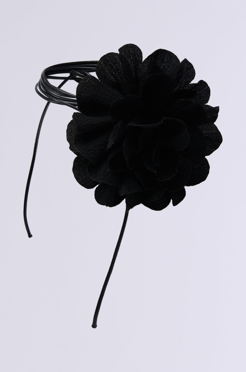 The FLOWER DREAMIN CORSAGE NECKLACE is a striking large black floral hair accessory with layered petals on a flexible band, complemented by two long black strings for an elegant and distinctive look against a simple white background. 1