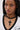 A woman with long straight hair exudes vampiress vibes, wearing large hoop earrings and the DOLCE NECKLACE—layered with a black cross pendant. She’s dressed in a white top with black trim, gazing slightly to the side.