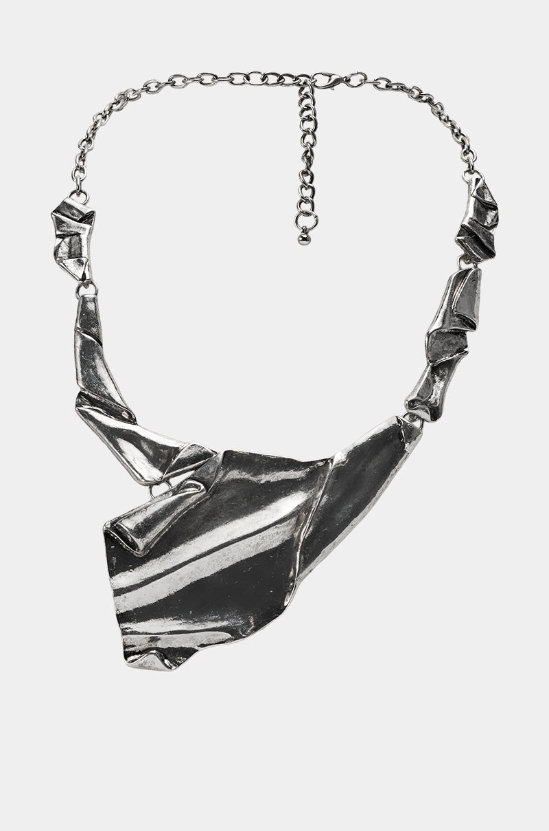 The BENT OUTTA SHAPE NECKLACE is a silver metallic piece featuring an abstract, angular design with folded geometric shapes linked together and a bold, large asymmetrical pendant as its centerpiece. 0