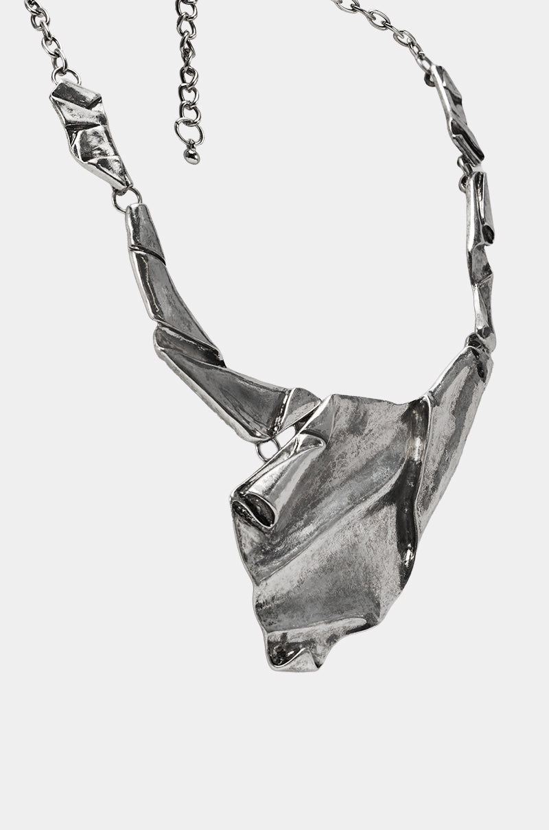 The BENT OUTTA SHAPE NECKLACE features a chunky silver metallic design with an abstract, crumpled metal pendant and geometric, angular chain links, shown against a white background. 3