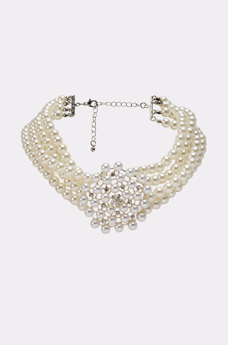The TRULY PEARL CHOKER is a multi-strand faux pearl necklace with a large, ornate floral centerpiece accented by clustered pearls and sparkling rhinestones, finished with an adjustable chain clasp. 1