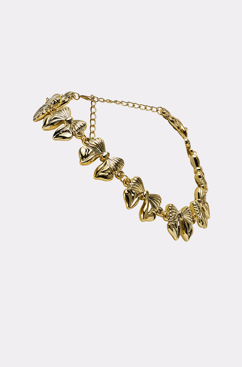 The BOW NECKLACE by AKIRA Label is a gold-tone piece featuring multiple bow-shaped charms and an adjustable chain clasp, shown on a plain light background. 2